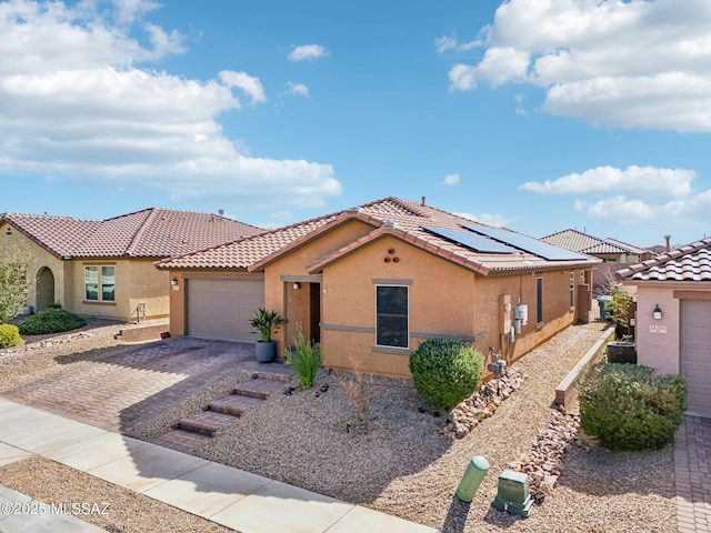 mediterranean / spanish home with a garage, roof mounted solar panels, decorative driveway, and stucco siding