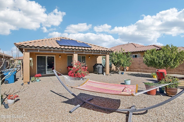 back of property with a tiled roof, fence private yard, a patio area, roof mounted solar panels, and stucco siding