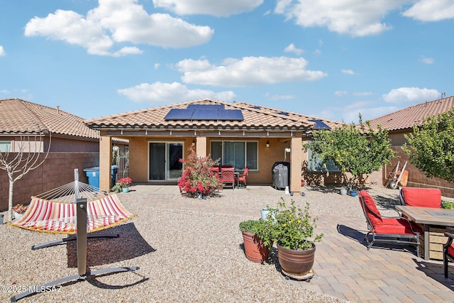 back of house with outdoor dining area, a patio area, solar panels, and stucco siding