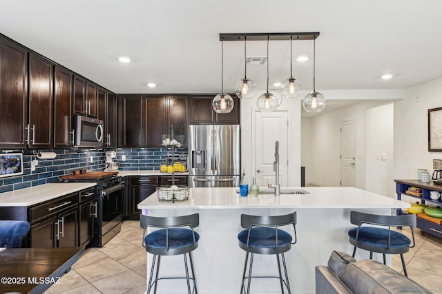 kitchen with decorative backsplash, appliances with stainless steel finishes, light countertops, a kitchen bar, and a sink