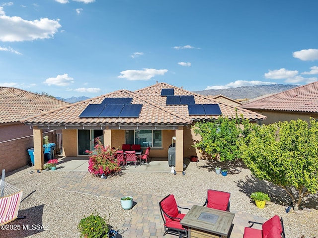 rear view of property with a tile roof, a patio, stucco siding, roof mounted solar panels, and a mountain view