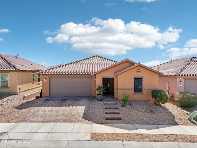 mediterranean / spanish-style home with a tiled roof, decorative driveway, an attached garage, and stucco siding