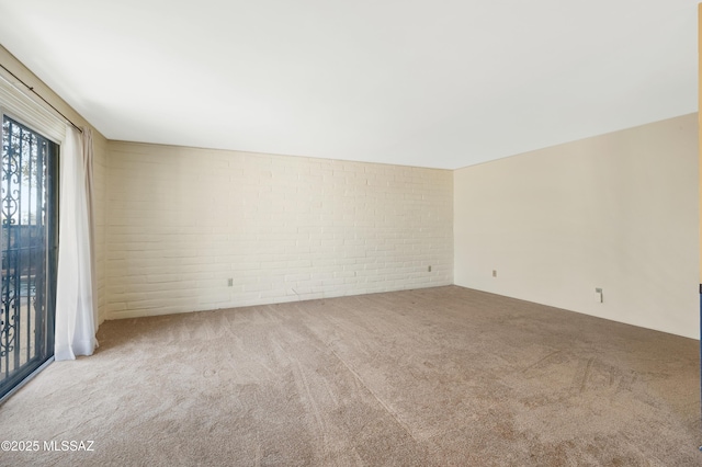 carpeted spare room featuring brick wall