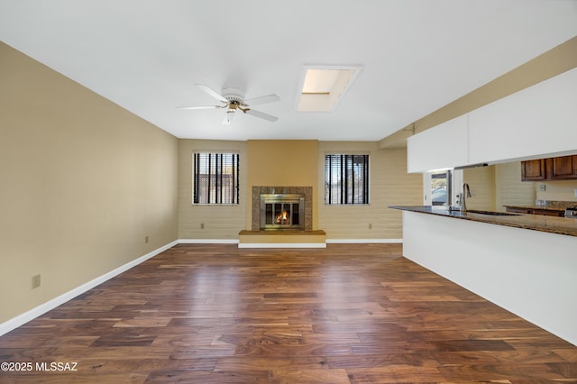 unfurnished living room with sink, ceiling fan, a skylight, a fireplace, and dark hardwood / wood-style flooring