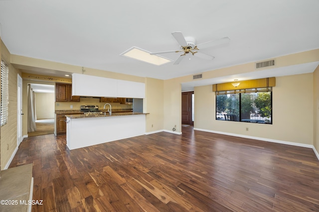 unfurnished living room featuring sink, dark wood-type flooring, ceiling fan, and a skylight