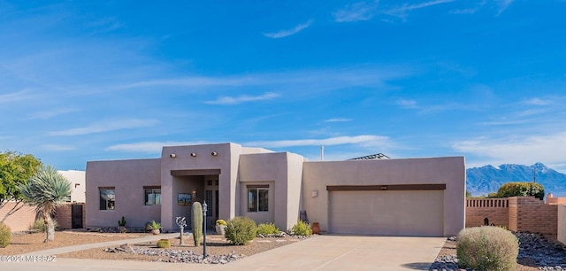 pueblo-style home featuring fence, concrete driveway, stucco siding, a garage, and a mountain view