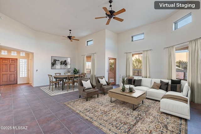 living area with dark tile patterned floors, a ceiling fan, a high ceiling, and a wealth of natural light