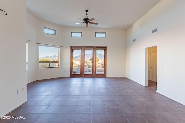 empty room featuring a high ceiling, dark tile patterned floors, visible vents, and ceiling fan