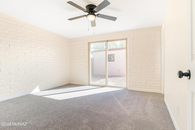 carpeted spare room with ceiling fan and brick wall