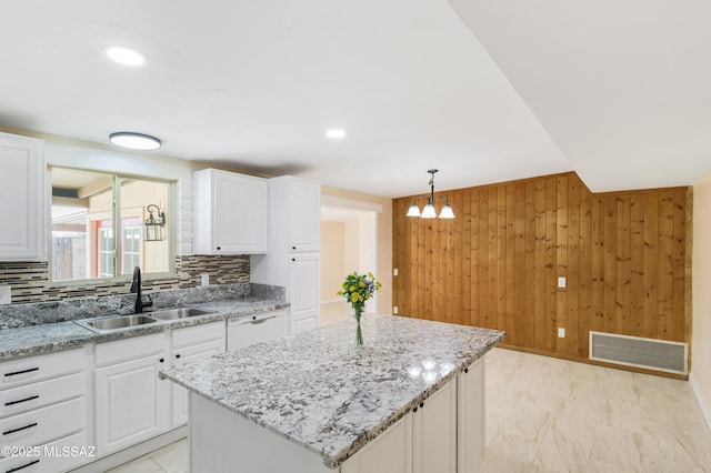 kitchen featuring sink, wood walls, white cabinetry, hanging light fixtures, and a kitchen island