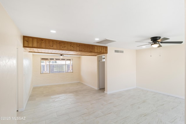 empty room featuring ceiling fan and brick wall