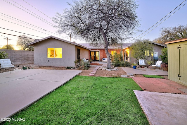 back house at dusk featuring a patio area and a lawn