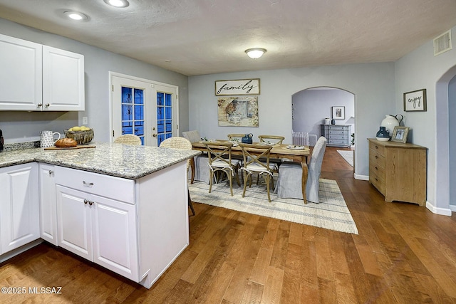 kitchen with french doors, white cabinetry, light stone counters, kitchen peninsula, and hardwood / wood-style flooring