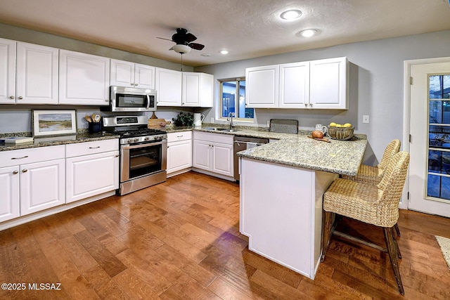 kitchen with white cabinetry, stainless steel appliances, a kitchen breakfast bar, light stone counters, and kitchen peninsula