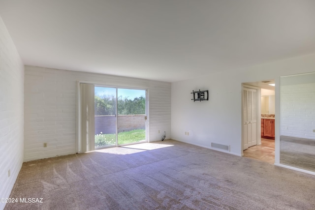 carpeted spare room with brick wall