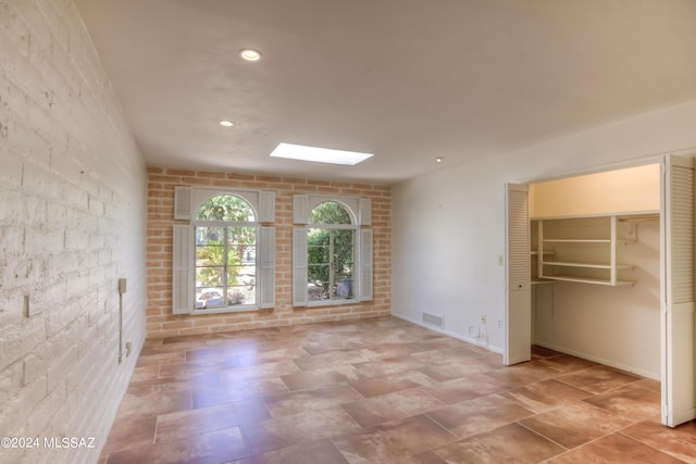 unfurnished room with brick wall and a skylight