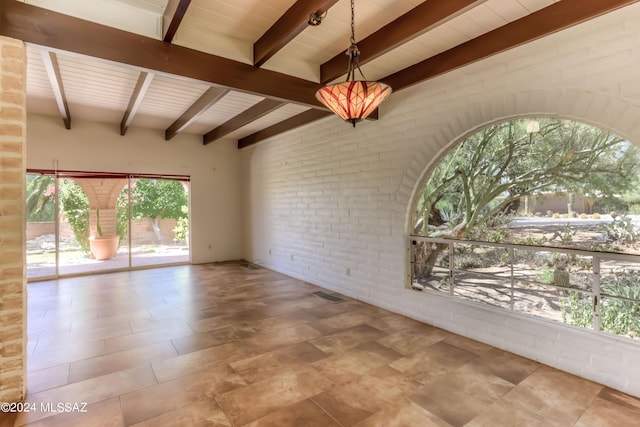 spare room with brick wall and beam ceiling