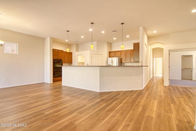 kitchen with decorative light fixtures, stainless steel fridge, double oven, stone counters, and light hardwood / wood-style floors