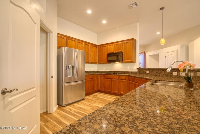 kitchen featuring sink, stainless steel fridge with ice dispenser, decorative light fixtures, dark stone counters, and light wood-type flooring