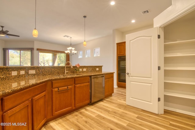 kitchen with sink, dark stone counters, hanging light fixtures, stainless steel dishwasher, and light wood-type flooring