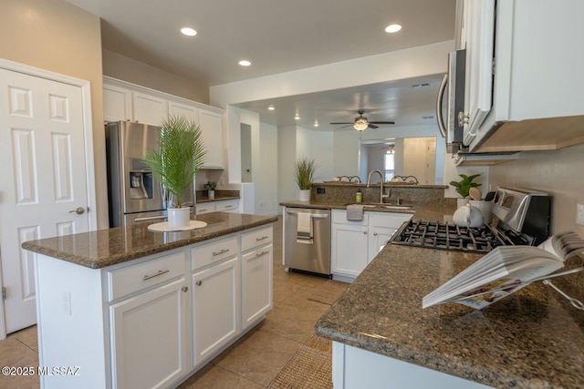 kitchen featuring appliances with stainless steel finishes, white cabinetry, sink, dark stone countertops, and a center island