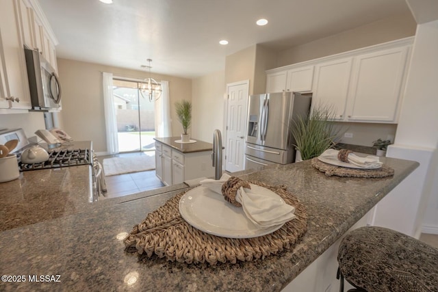 kitchen featuring white cabinetry, a chandelier, appliances with stainless steel finishes, kitchen peninsula, and dark stone counters