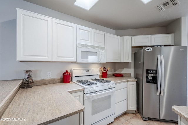 kitchen with light tile patterned flooring, white cabinets, white appliances, and a skylight