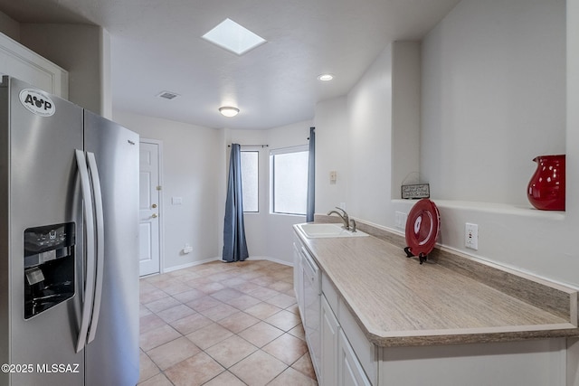 kitchen featuring sink, light tile patterned floors, stainless steel fridge, a skylight, and white cabinets