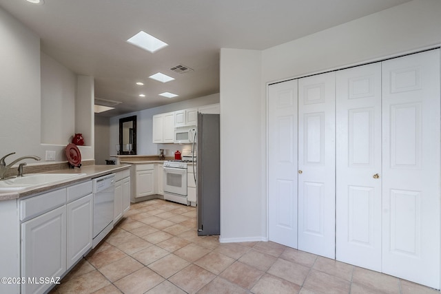 kitchen with sink, white appliances, white cabinetry, light tile patterned flooring, and kitchen peninsula