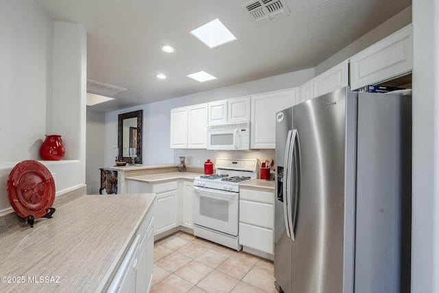 kitchen featuring white cabinetry, a skylight, light tile patterned floors, kitchen peninsula, and white appliances