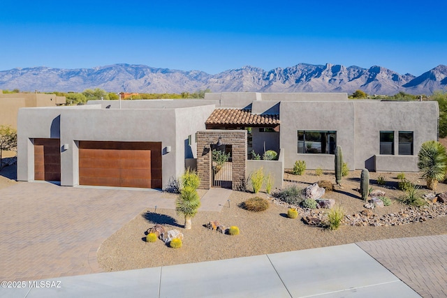 adobe home with decorative driveway, a mountain view, an attached garage, and stucco siding