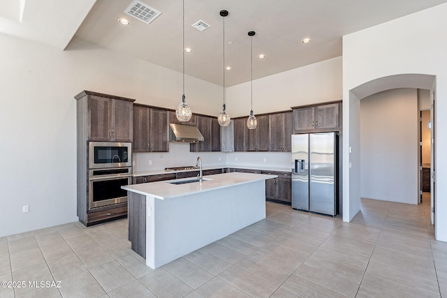 kitchen with stainless steel appliances, light countertops, hanging light fixtures, an island with sink, and under cabinet range hood