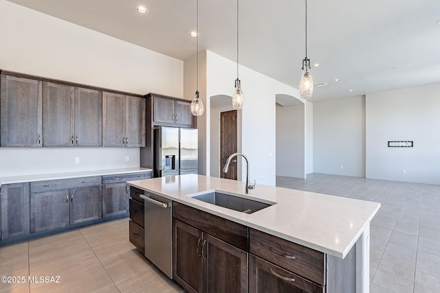 kitchen featuring a center island with sink, hanging light fixtures, appliances with stainless steel finishes, a sink, and dark brown cabinets