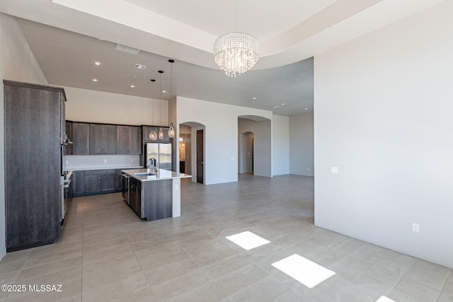 kitchen featuring open floor plan, light countertops, hanging light fixtures, stainless steel fridge, and a center island with sink