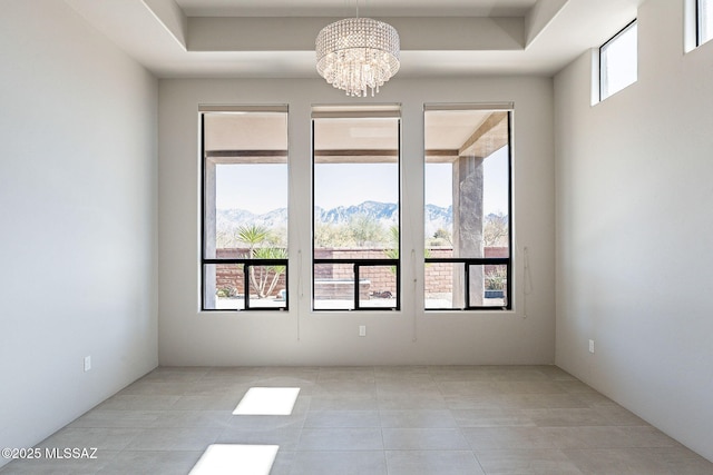 spare room with plenty of natural light, a mountain view, a raised ceiling, and a notable chandelier