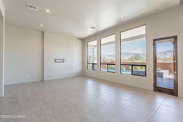 empty room featuring a healthy amount of sunlight, light tile patterned floors, visible vents, and a mountain view