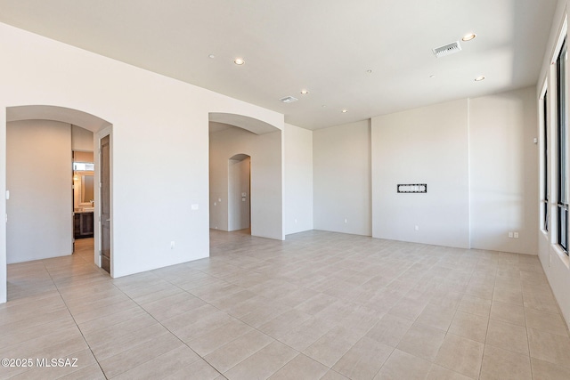 unfurnished room with light tile patterned floors, arched walkways, visible vents, and recessed lighting