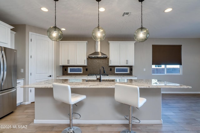 kitchen with stainless steel refrigerator, an island with sink, and pendant lighting