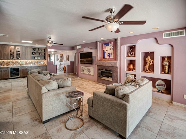 living room featuring built in features, a fireplace, visible vents, beverage cooler, and bar