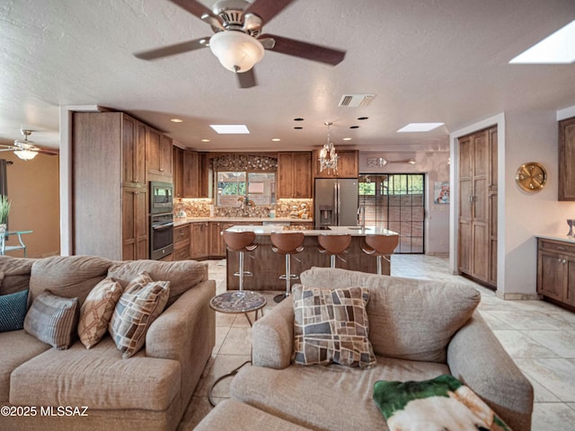 living room featuring a skylight, visible vents, a textured ceiling, and light tile patterned floors