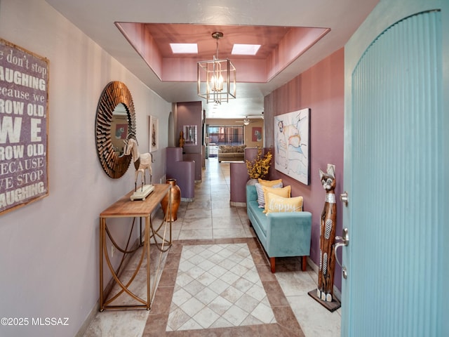 hallway featuring a skylight, baseboards, a tray ceiling, and light tile patterned flooring