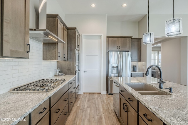 kitchen featuring sink, appliances with stainless steel finishes, hanging light fixtures, light stone countertops, and wall chimney exhaust hood