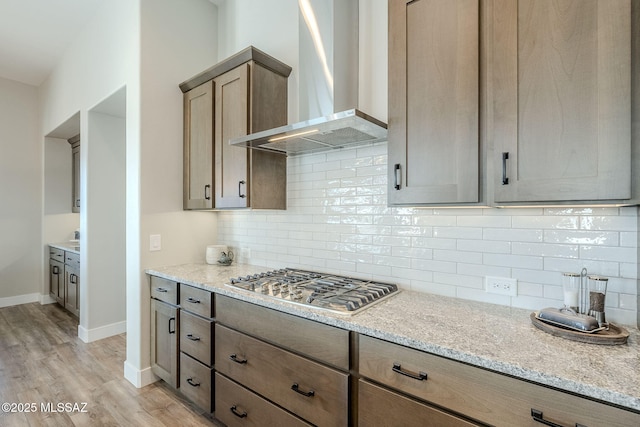 kitchen featuring stainless steel gas stovetop, light wood-type flooring, wall chimney range hood, and light stone counters