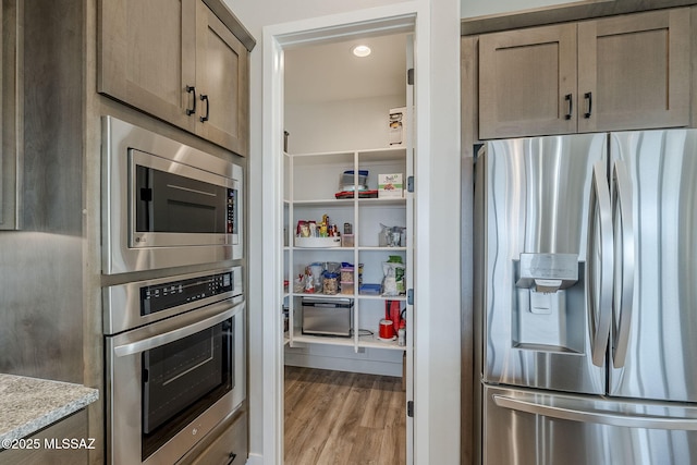 kitchen with light stone countertops, appliances with stainless steel finishes, and light hardwood / wood-style floors