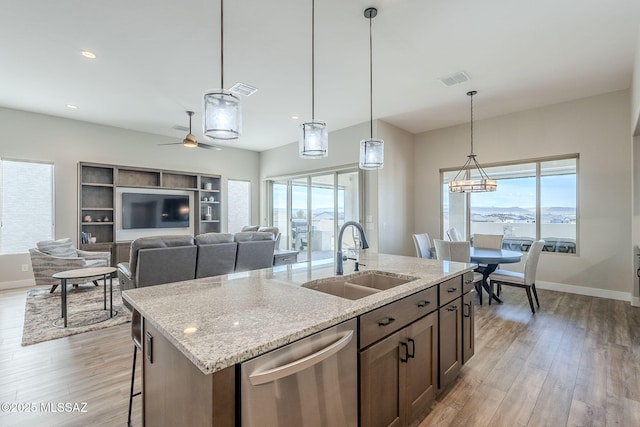 kitchen with decorative light fixtures, an island with sink, sink, stainless steel dishwasher, and light stone counters