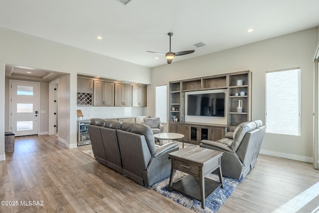 living room featuring wine cooler, light wood-type flooring, ceiling fan, and bar area