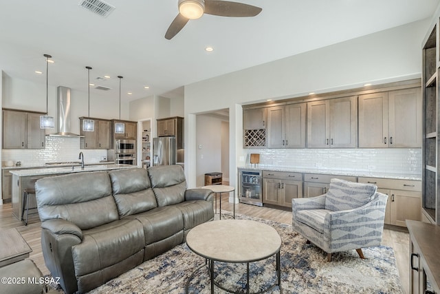 living room featuring ceiling fan, bar area, beverage cooler, and light wood-type flooring