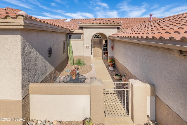 entrance to property featuring a tiled roof, a gate, fence, and stucco siding