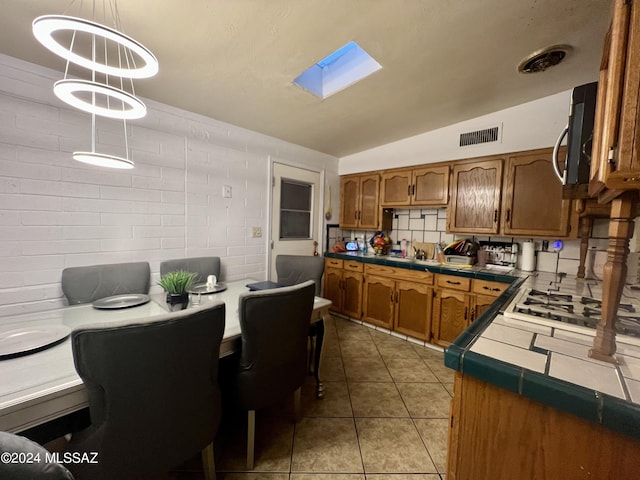 kitchen featuring vaulted ceiling with skylight, tile countertops, hanging light fixtures, and light tile patterned floors