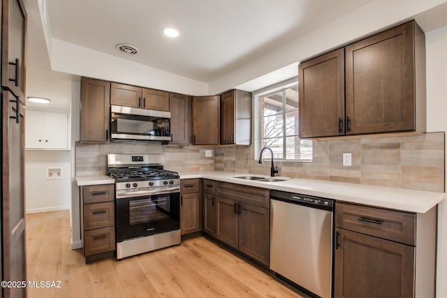 kitchen with appliances with stainless steel finishes, sink, dark brown cabinetry, and light wood-type flooring